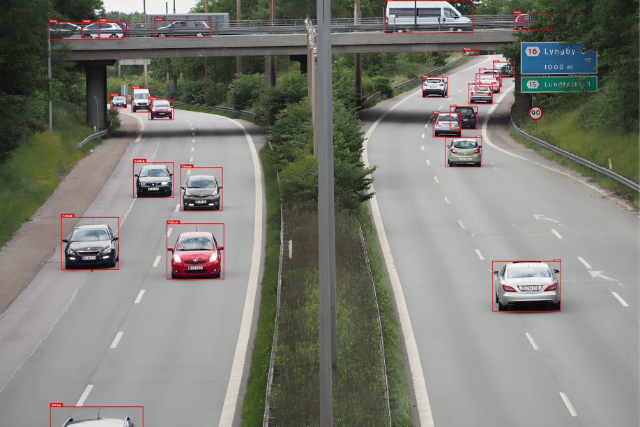 A highway scene showing multiple cars driving in both directions, each enclosed with red bounding boxes for object detection. The image includes vehicles on the main road and an overpass, with clear lane markings, road signs, and greenery on both sides. The bounding boxes indicate an AI-based vehicle detection or data annotation process.